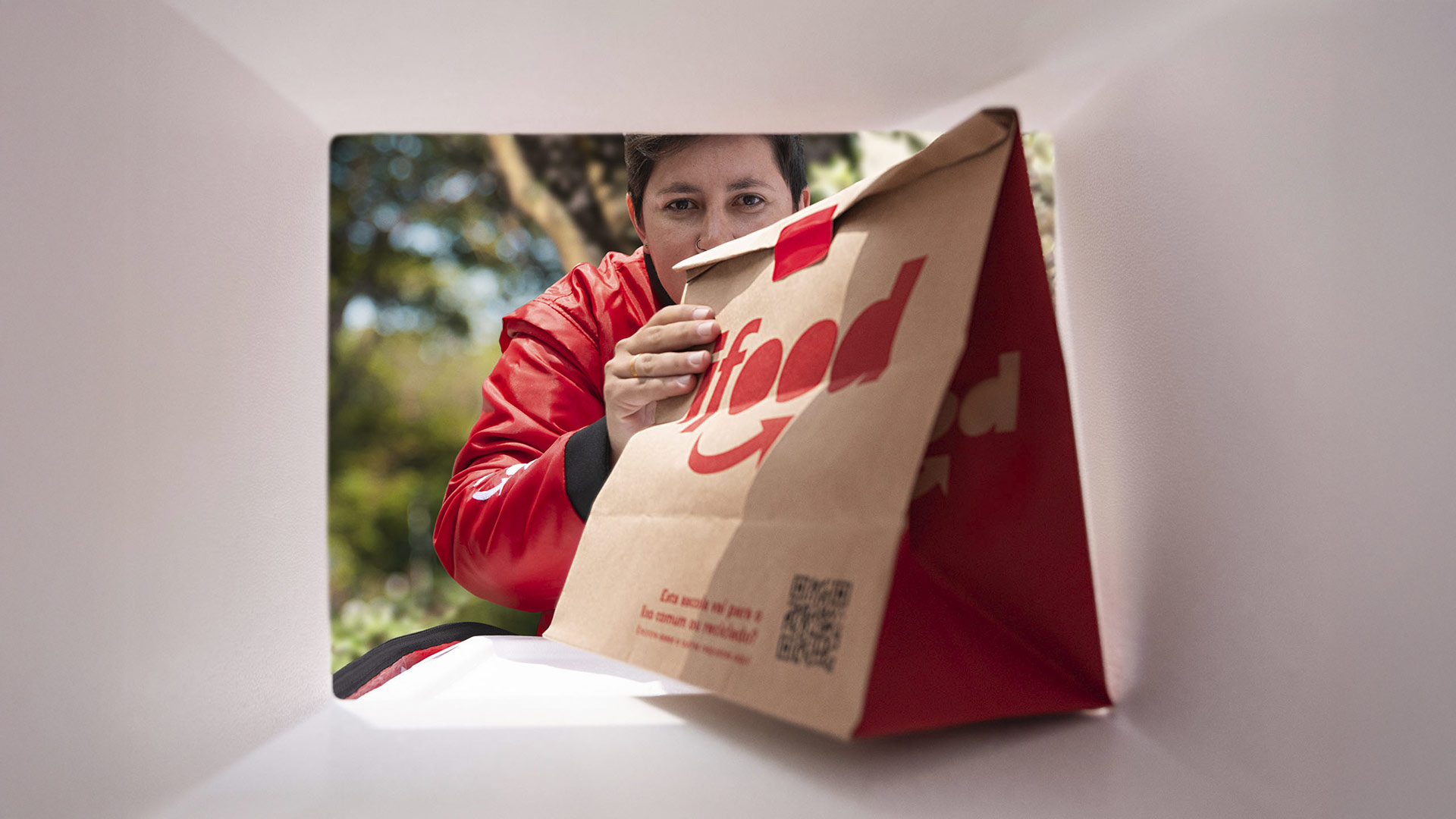 Pessoa entregadora segurando um pedido com embalagem do iFood dentro de uma bolsa térmica.