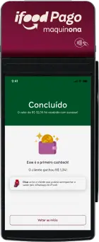 Foto da maquininha de cartão "iFood Pago maquinona". A tela exibe a confirmação de um pagamento de R$ 32,00 com a mensagem "Concluído" e anuncia o primeiro cashback do cliente no valor de R$ 1,34.